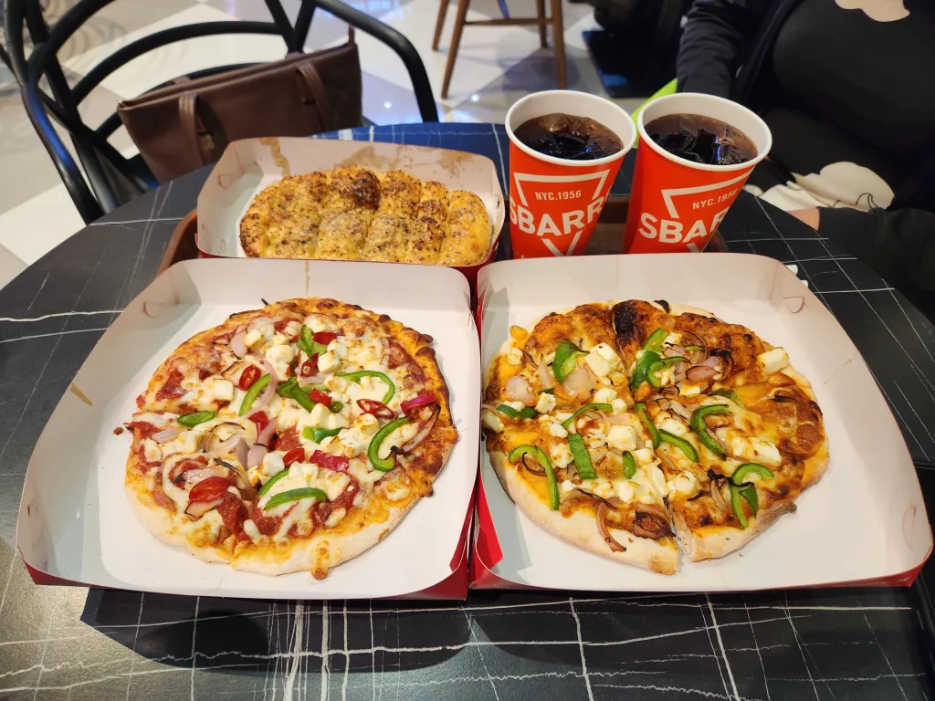 Pizza meal with two pizzas, garlic bread, and cold drinks on a table.