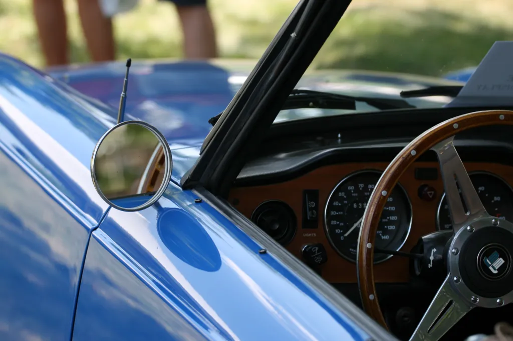 A blue vintage car with a wooden steering wheel and a round side mirror.
