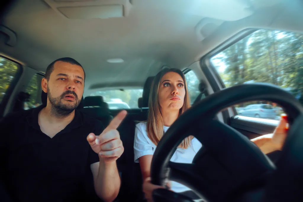 A man in the passenger seat points while a woman with an anxious expression drives.