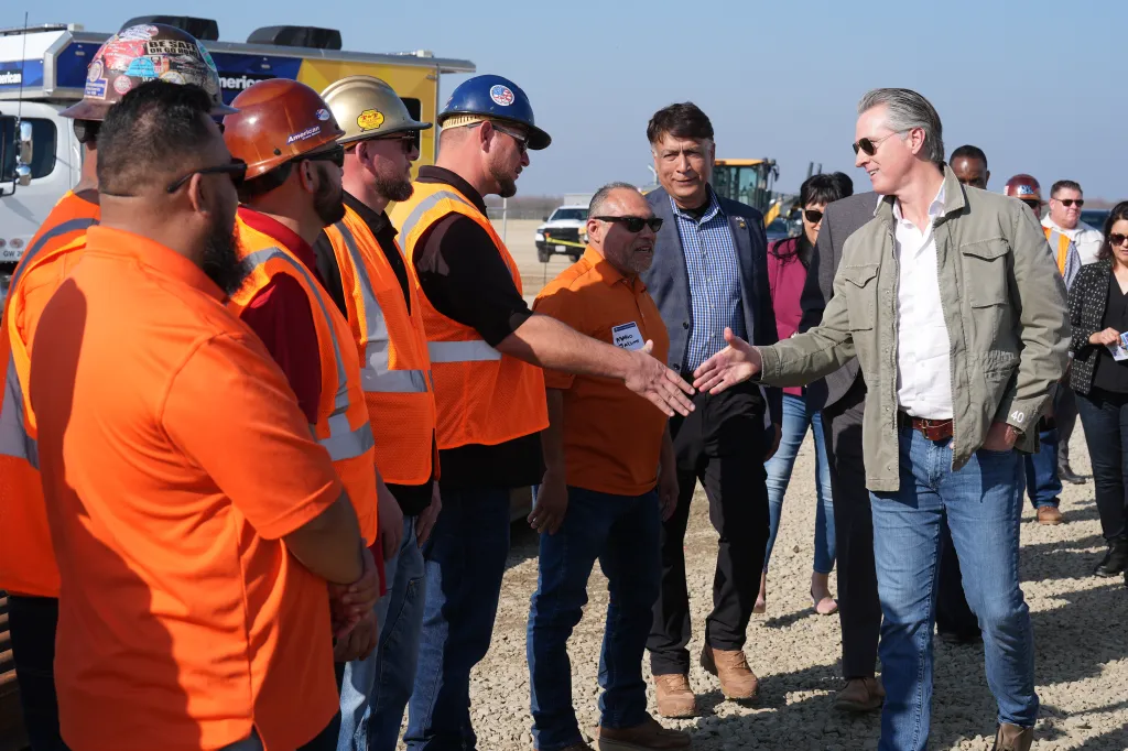 California Gov. Gavin Newsom shaking hands with an Iron Workers Local 155 worker as Ian Choudri, CEO for the California High-Speed Rail Authority, watches.