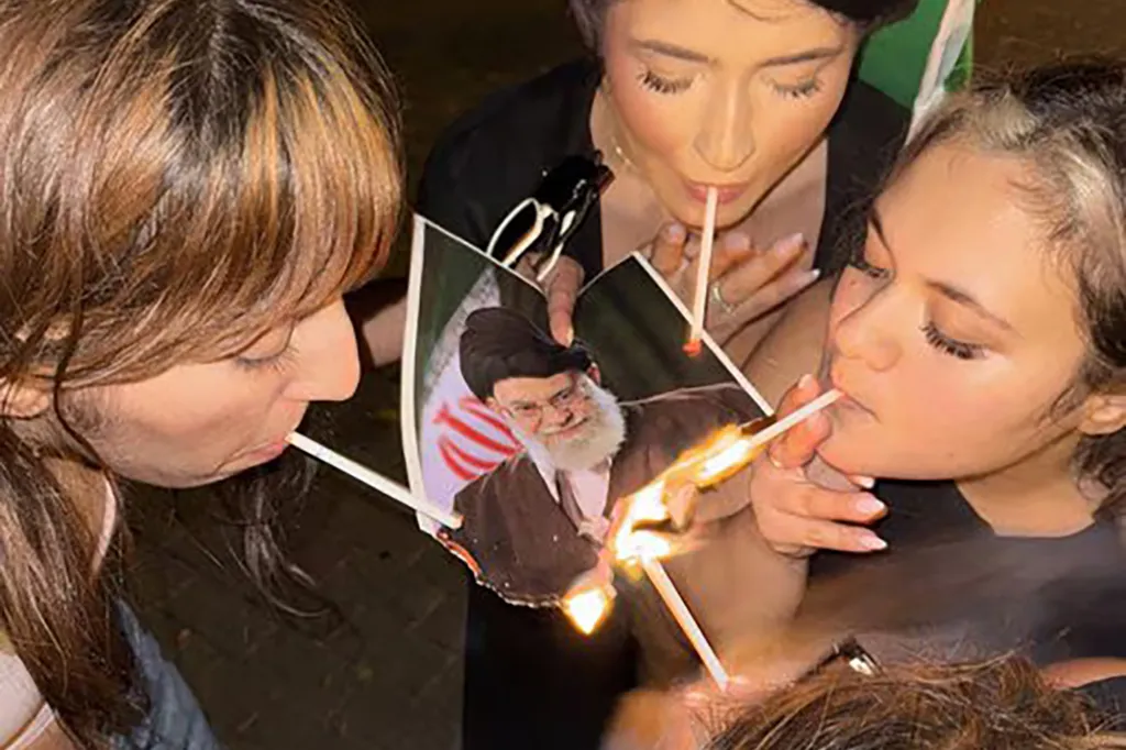 Three women use matches to burn a photo of Iran’s Supreme Leader Ali Khamenei.