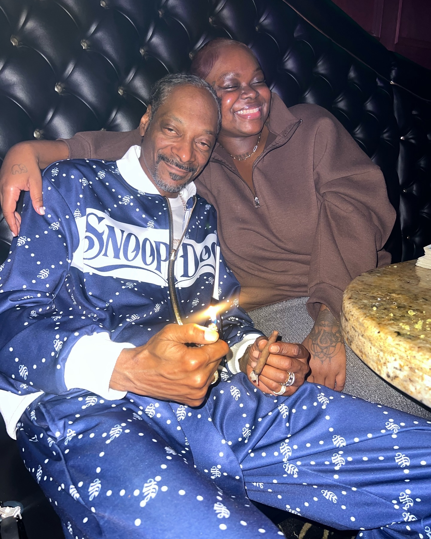 Snoop Dogg and his daughter Cori Broadus sit closely in a booth, with Cori's arm around her father.