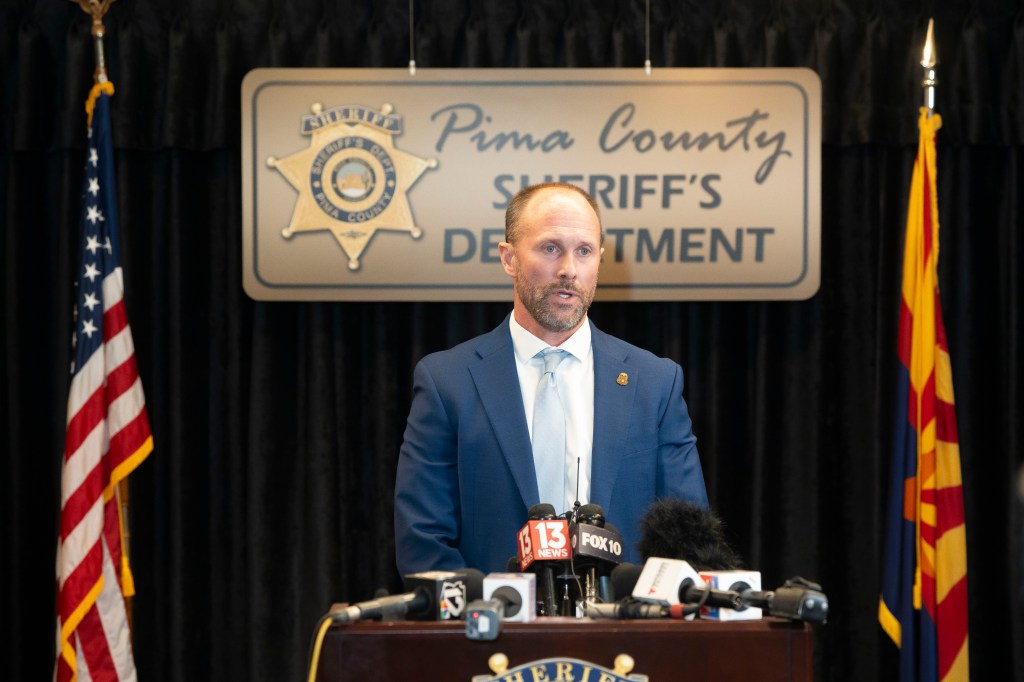 Pima County Sheriff Chris Nanos speaks at a press conference with news microphones in front of him.