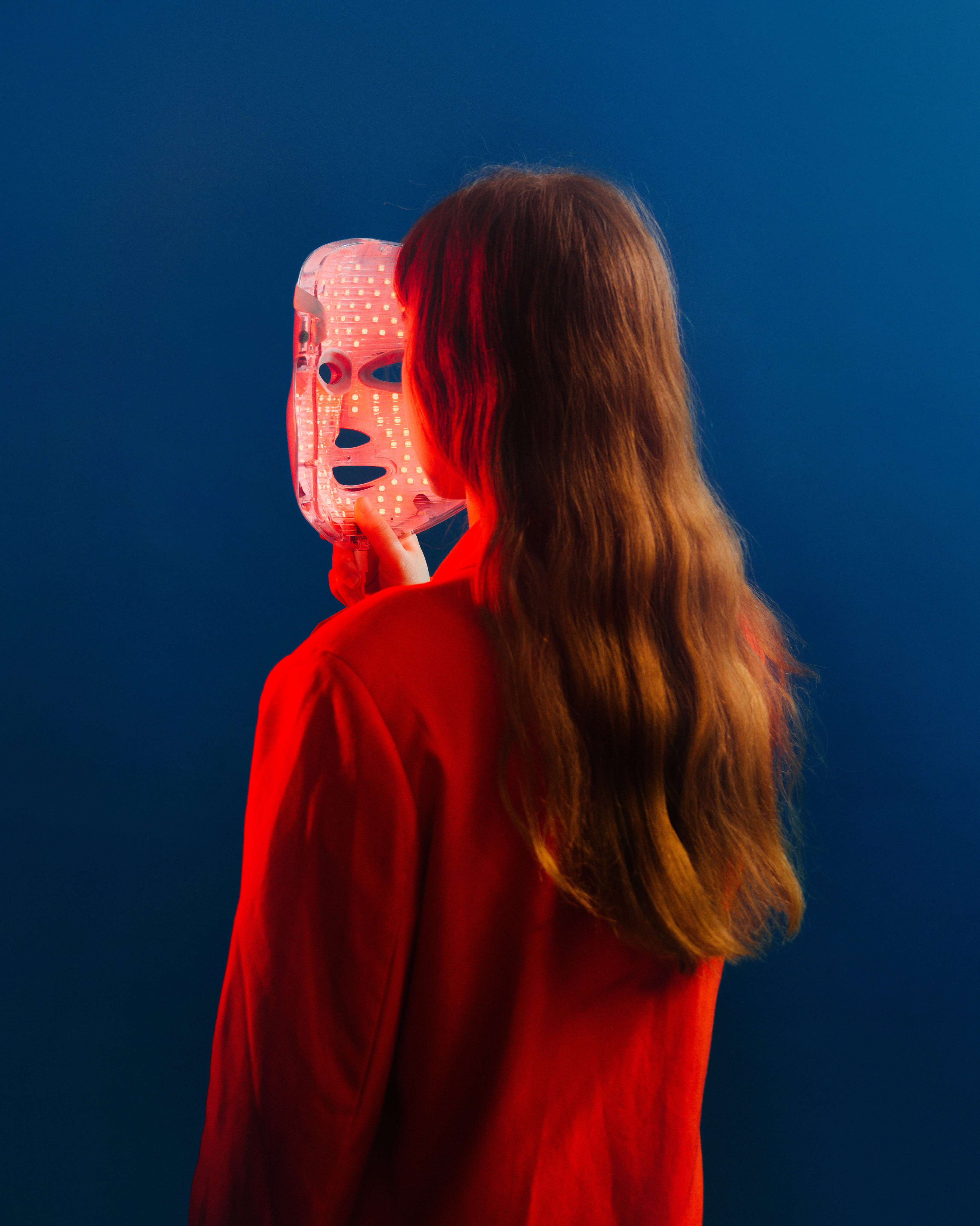 A color photograph of a woman with an led light mask in front of her face