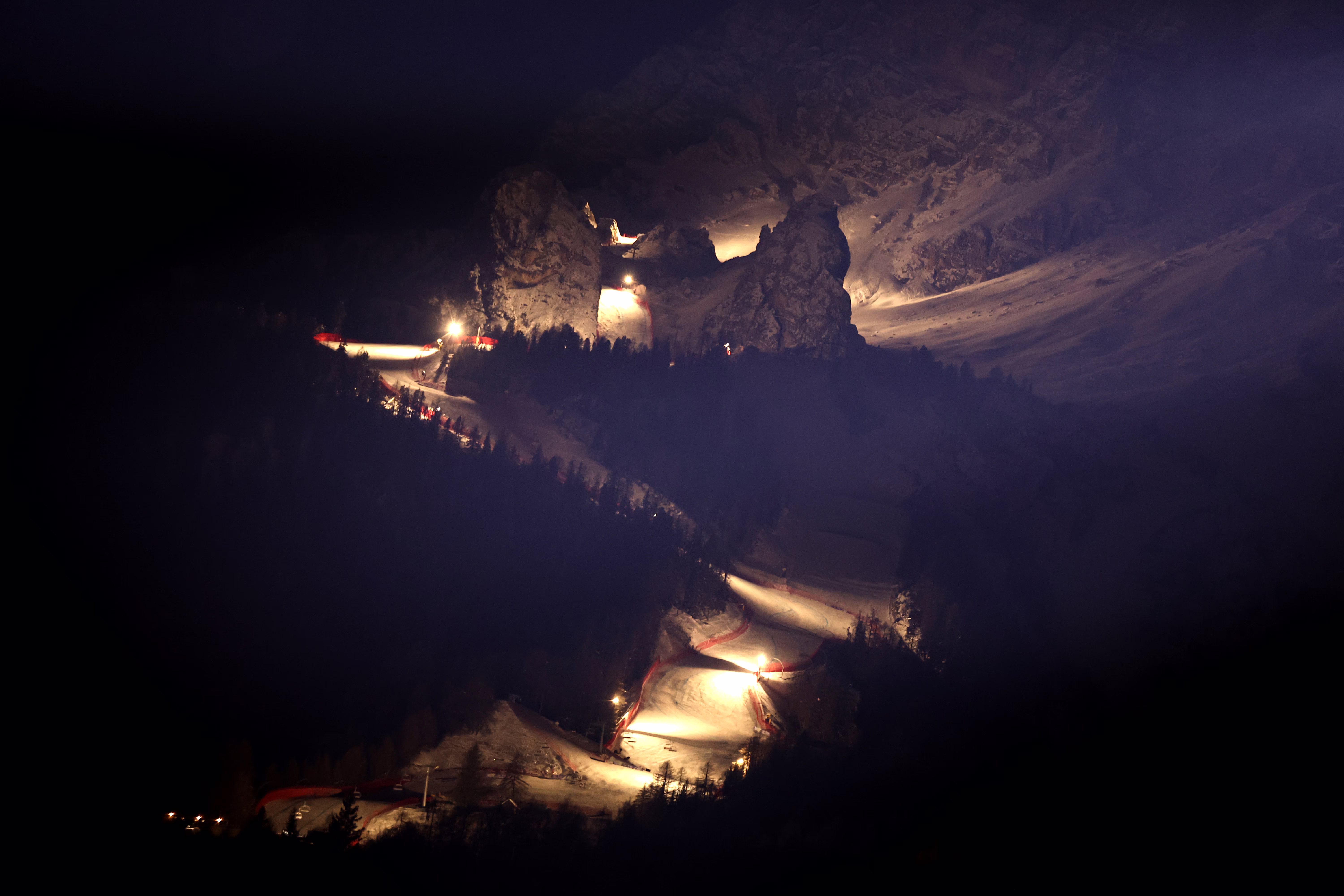 A night view of an Alpine ski run, lit by floodlights on the course.