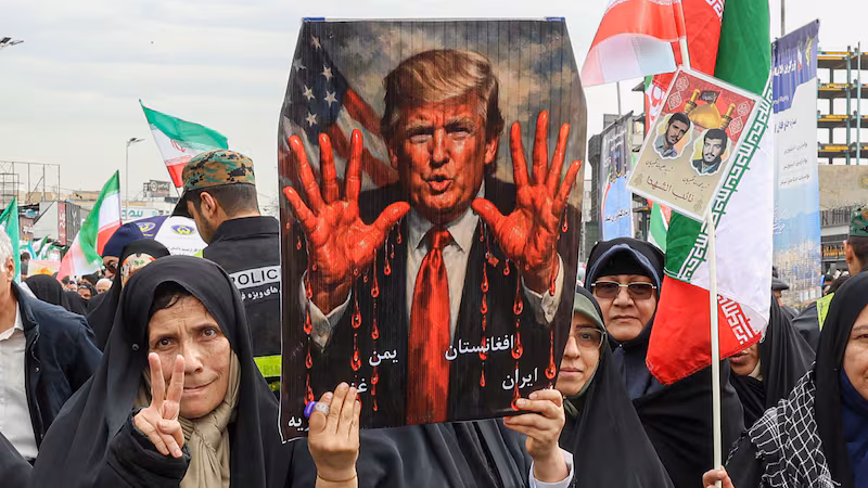 TOPSHOT - Women march with a sign depicting US President Donald Trump with bloodied hands in Tehran on February 11, 2026, during a rally marking the 47th anniversary of the 1979 Islamic revolution. The Persian calendar date of Bahman 22 celebrates the anniversary of the resignation of the ousted shah's last prime minister and the formal assumption of power by revolutionary leader Ayatollah Ruhollah Khomeini. (Photo by AFP via Getty Images)