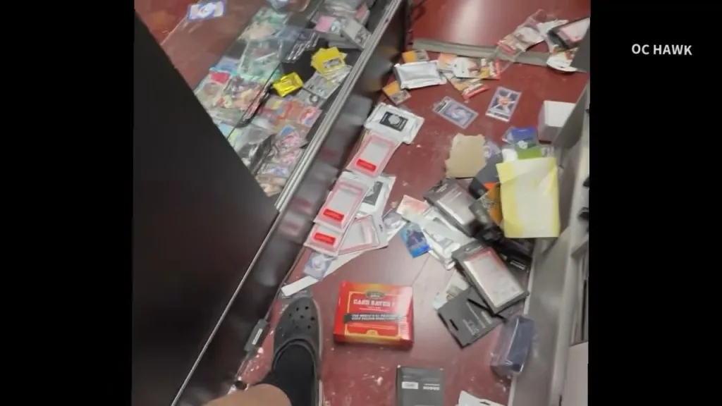 Messy aftermath of a theft, showing trading card merchandise scattered across the floor and display cases.