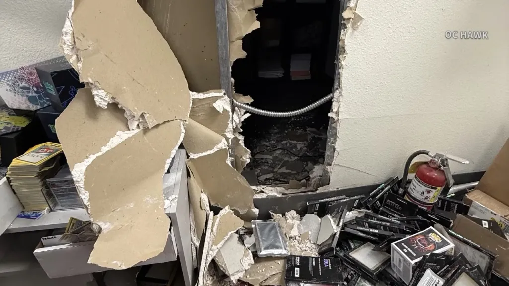 A large hole torn into a drywall with Pokémon cards and a fire extinguisher on the floor.