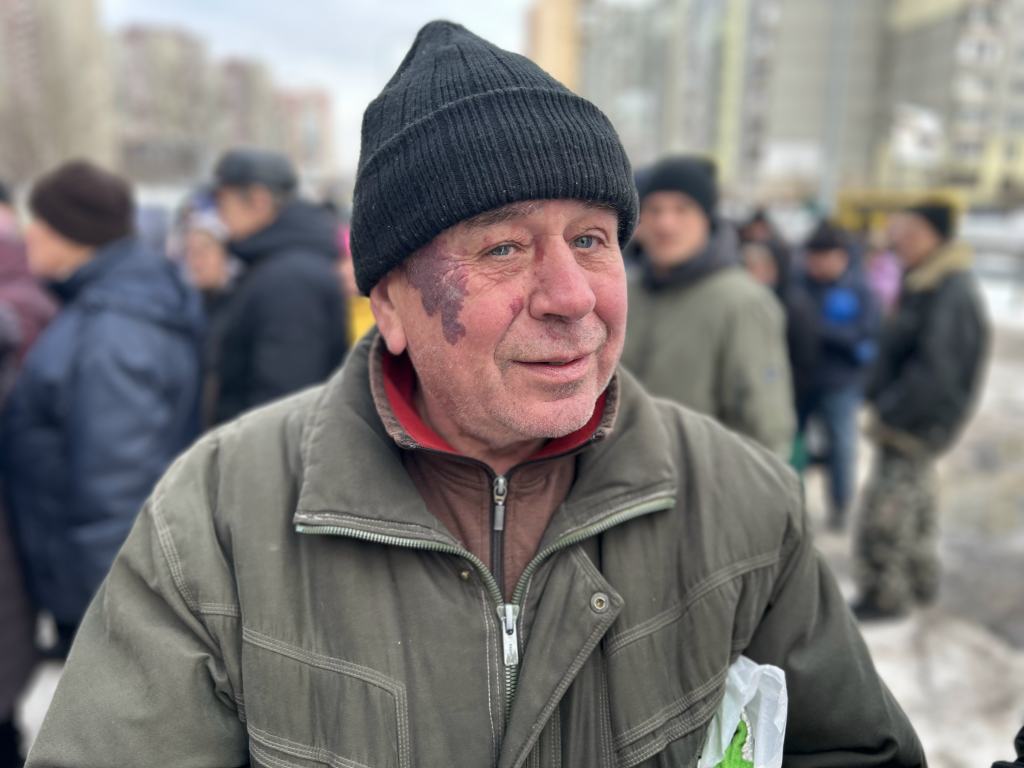 Anatoly, a 67-year-old locksmith with a bruised face, wearing a black knit cap and olive-green jacket, picks up soup from World Central Kitchen in Kyiv.