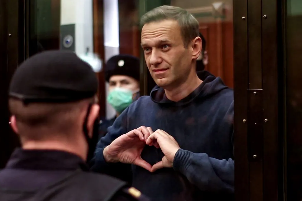 Alexei Navalny in a glass cell, making a heart shape with his hands.