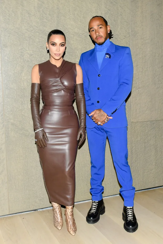 Kim Kardashian in a brown leather dress and Lewis Hamilton in a blue suit and turtleneck.