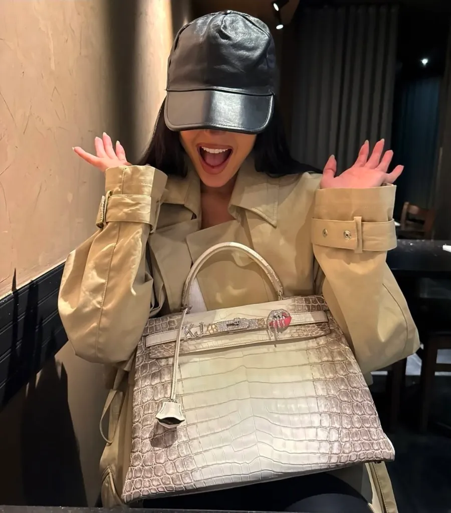 Kylie Jenner smiling and holding a crocodile Birkin bag.