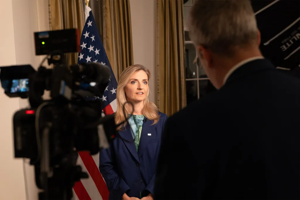 Under Secretary Rogers speaking into a microphone with an American flag behind her.