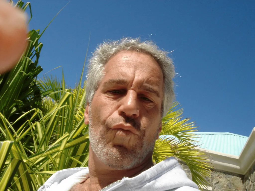Jeffrey Epstein is shown in a selfie with green tropical plants and a blue sky behind him.