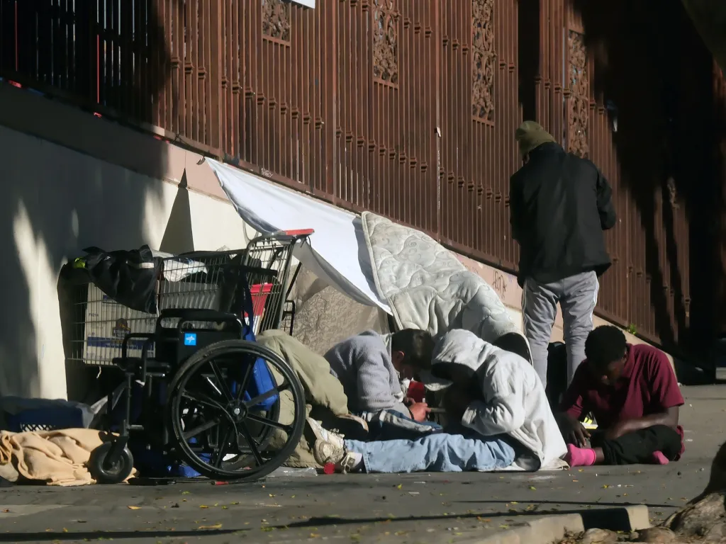 A homeless encampment with people, a shopping cart, and a wheelchair.