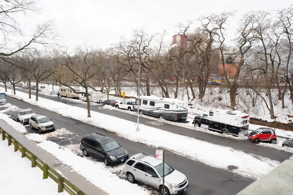 An encampment of campers and RVs lines a snow-covered street next to bare trees in the Bronx.