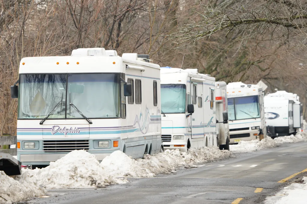 A line of RVs and campers parked on the side of a road with piles of snow next to them.