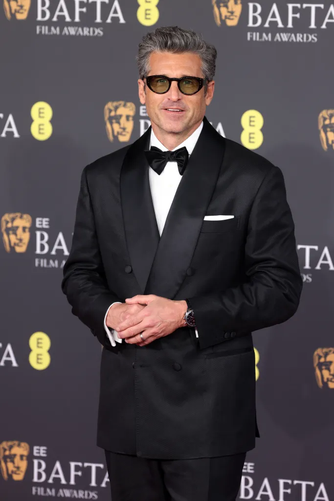 Patrick Dempsey on the red carpet at the EE BAFTA Film Awards, wearing a black tuxedo, bow tie, and sunglasses.