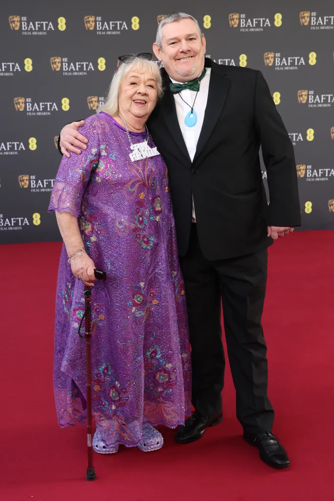 John Davidson and an elderly woman pose together on the red carpet at the BAFTA Film Awards.