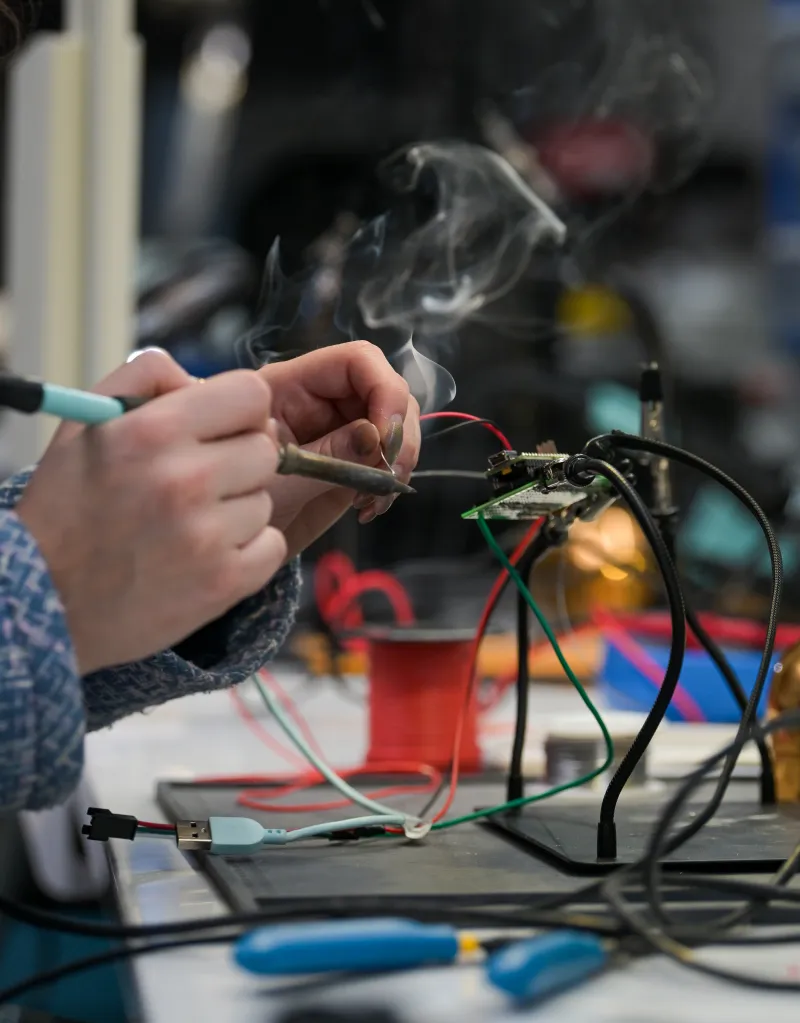 Hands soldering wires to a circuit board for robotic fashion.