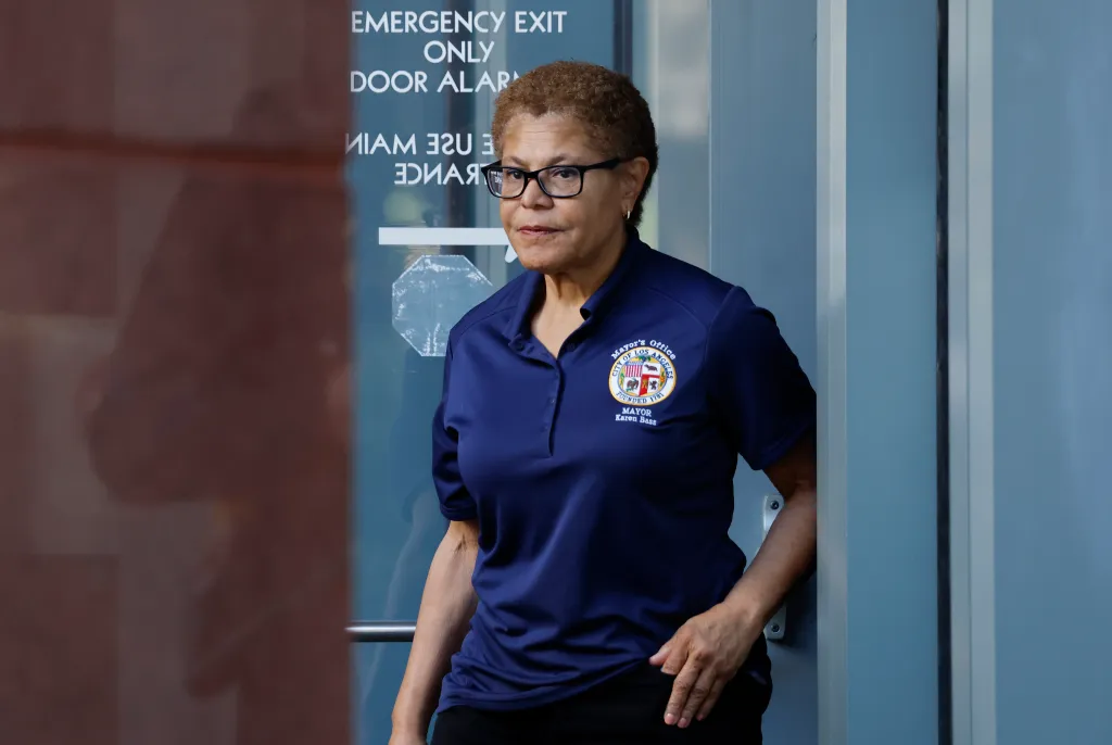 Los Angeles Mayor Karen Bass in a navy polo shirt with the city seal and her name, standing near a door.