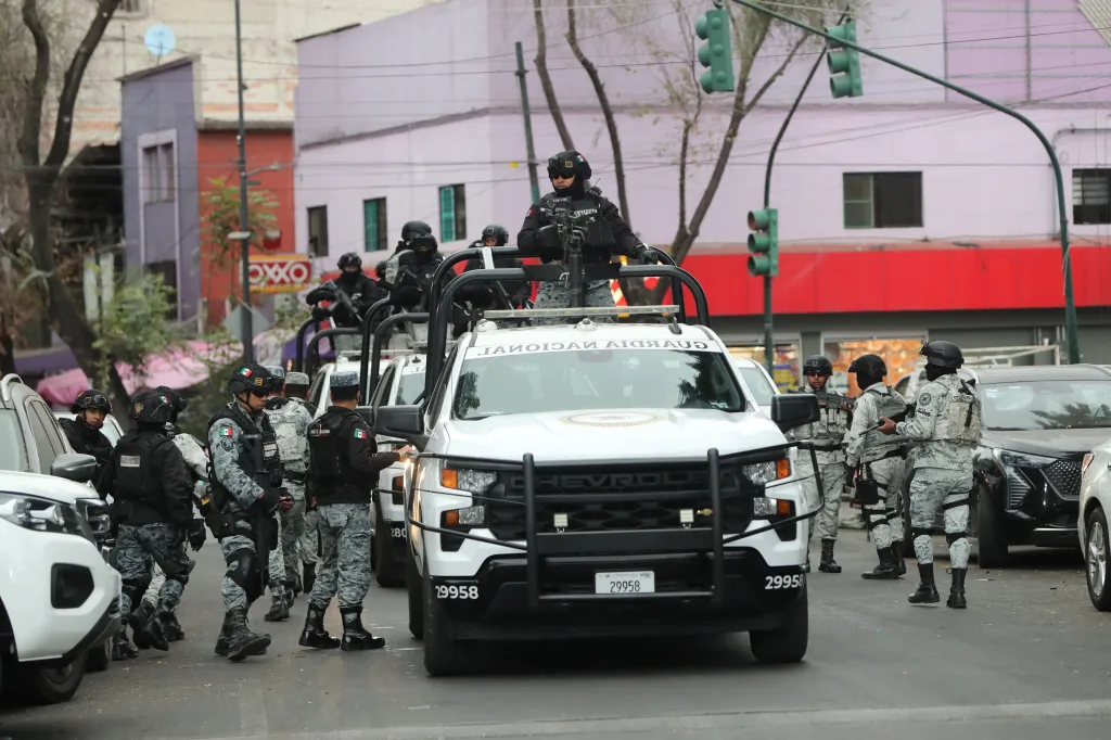 Mexican National Guard members in combat gear stand in and around white pickup trucks.