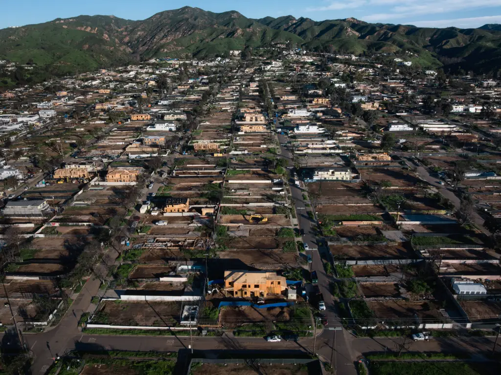 Aerial view of a fire-ravaged neighborhood in Pacific Palisades, California, showing homes being reconstructed.