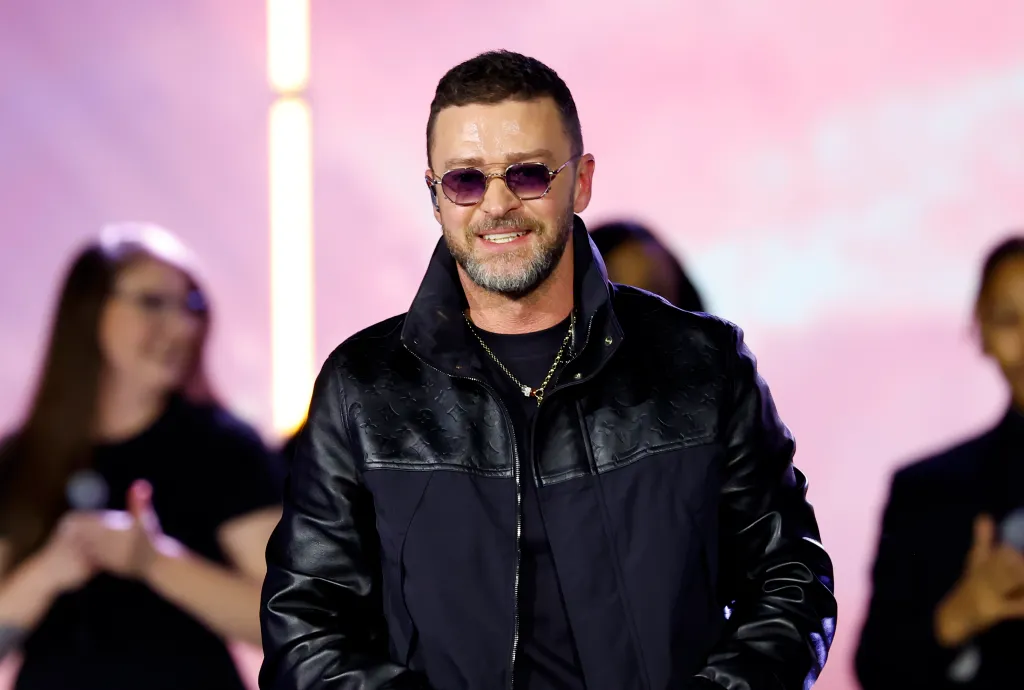 Justin Timberlake wearing sunglasses and a black jacket, smiling.