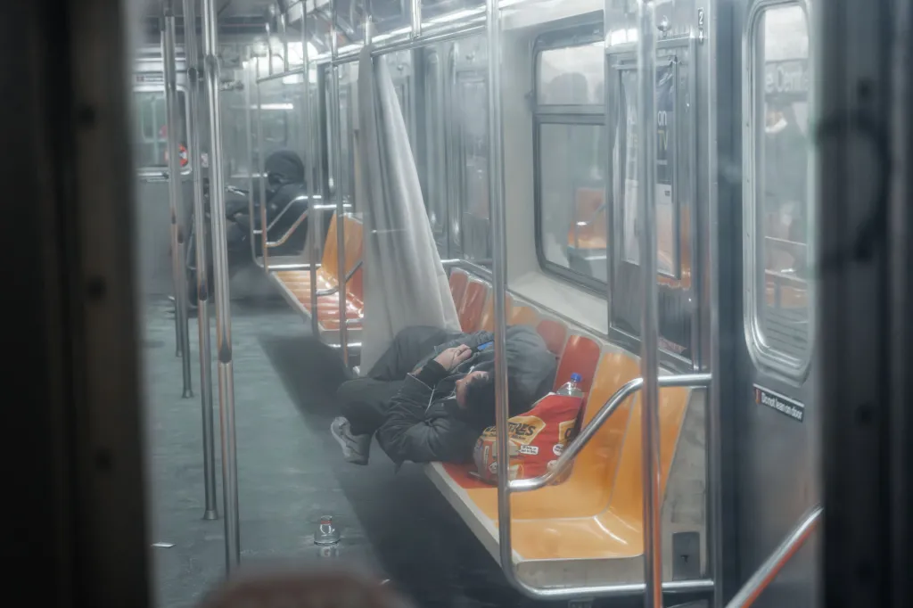 An unhoused person sleeps on subway seats in a train car during cold weather.