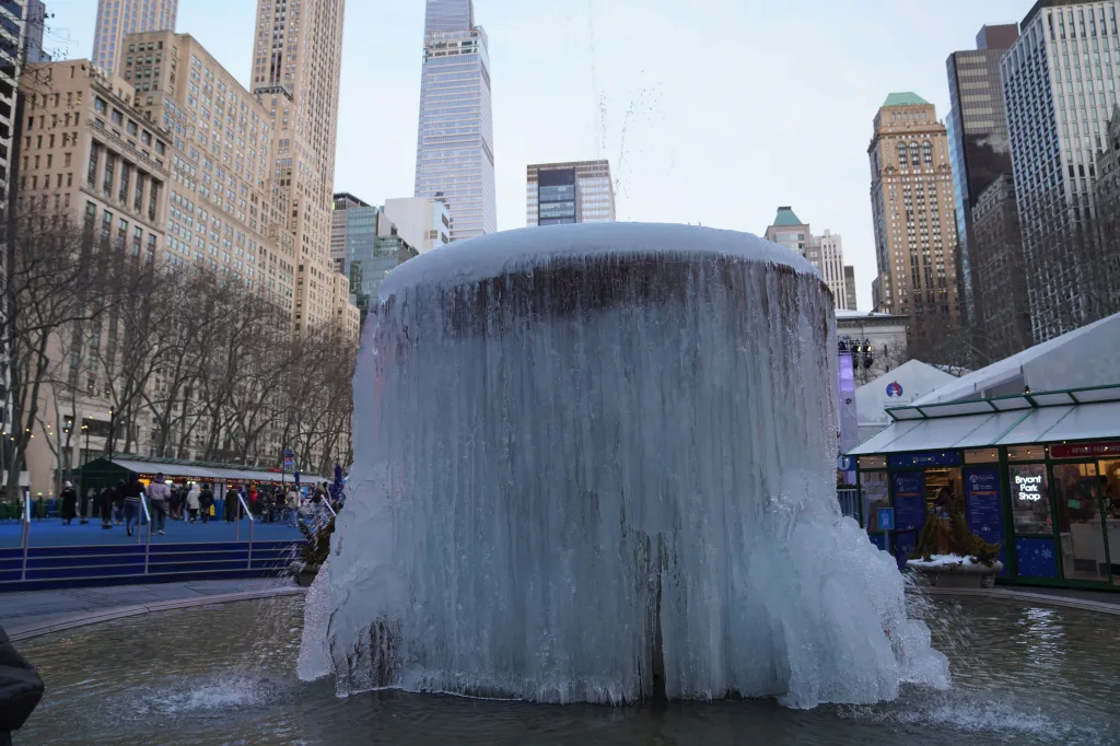 An iced fountain in New York City with skyscrapers and bare trees in the background.