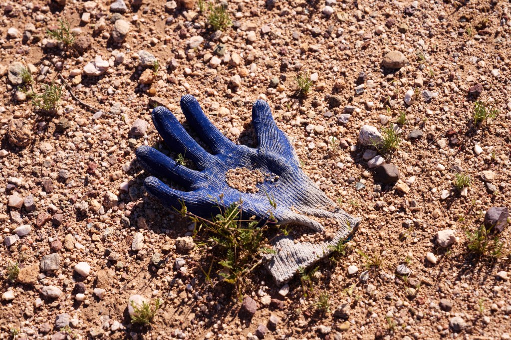 A discarded blue work glove lies on the ground in the desert, partially covered in dirt and small rocks.