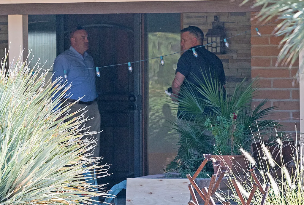 Two men, one in a blue shirt and one in a black shirt, stand on a porch.