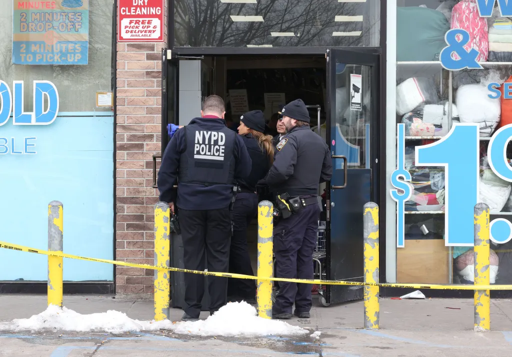 NYPD officers stand at the entrance of a Wash & Fold Super Laundry where a male was shot in the head.
