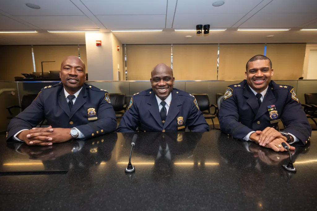 Three NYPD officers, Aaron Edwards, Benjamin Gurley, and Christopher Mcintosh, smiling and sitting at a conference table.