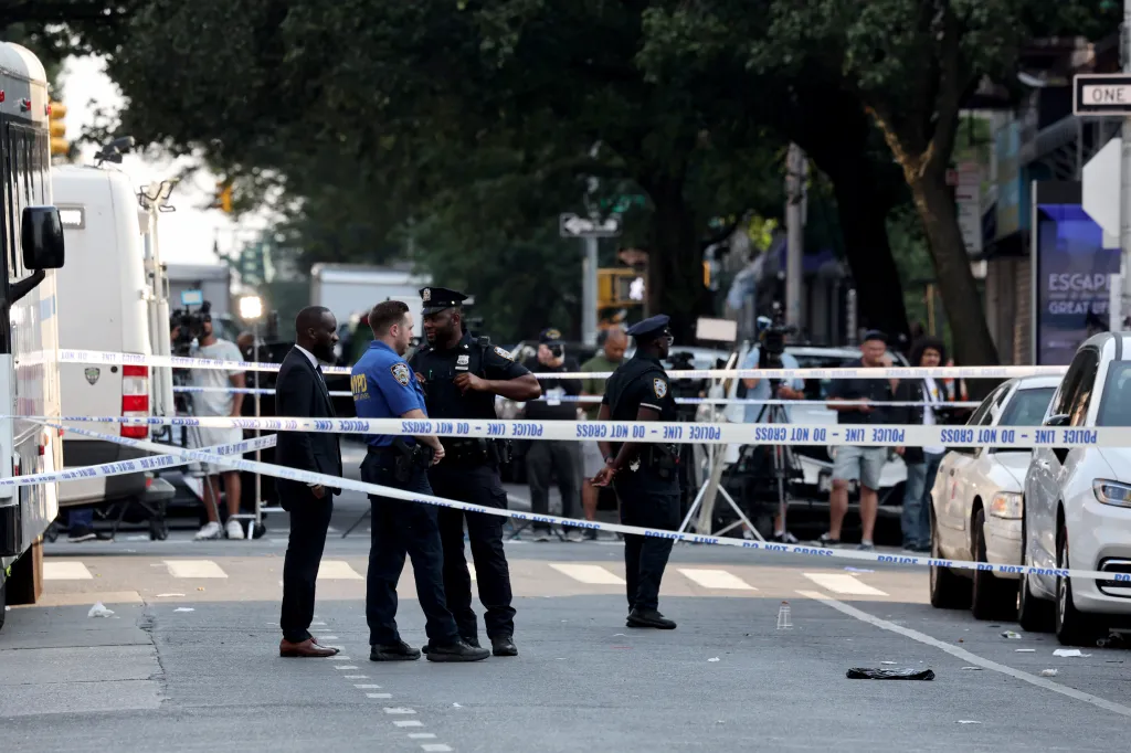 NYPD officers and detectives stand behind police tape at the scene of a mass shooting.