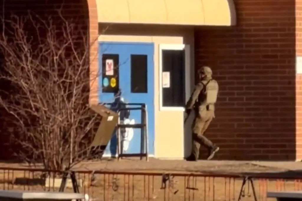 A person in tactical gear stands outside a blue door, holding a protective shield.