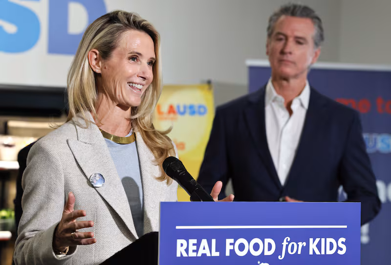 LOS ANGELES, CALIFORNIA - OCTOBER 08: California Governor Gavin Newsom looks on as his wife Jennifer Siebel Newsom speaks at Belvedere Middle School before he signed legislation aimed at improving kids' nutrition and health across California on October 8, 2025 in Los Angeles, California. The bill bans ultra-processed foods (UPFs) from school meals in the state. (Photo by