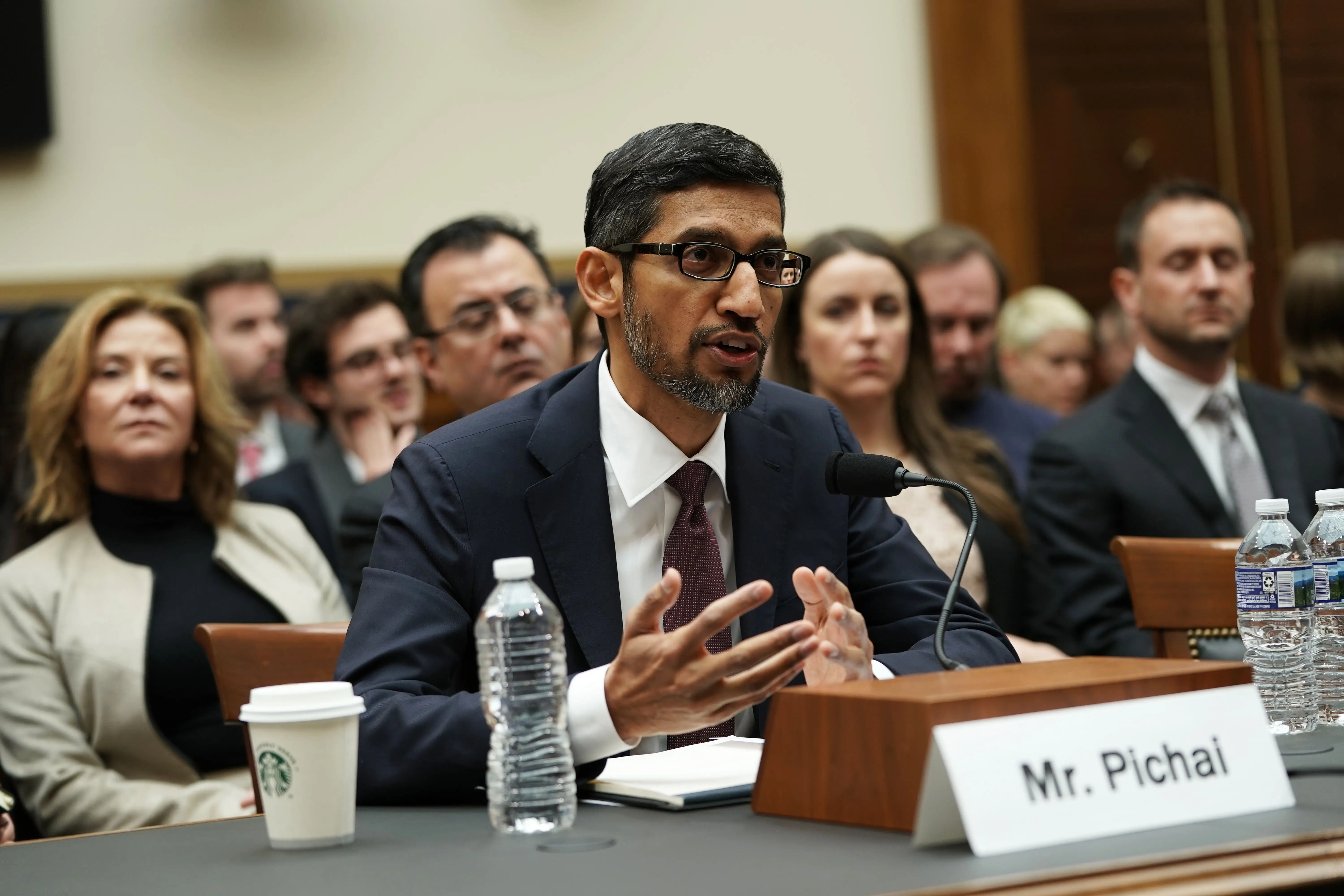 Google CEO Sundar Pichai sits at a table while testifying to Congress, while an audience sits behind him to watch.