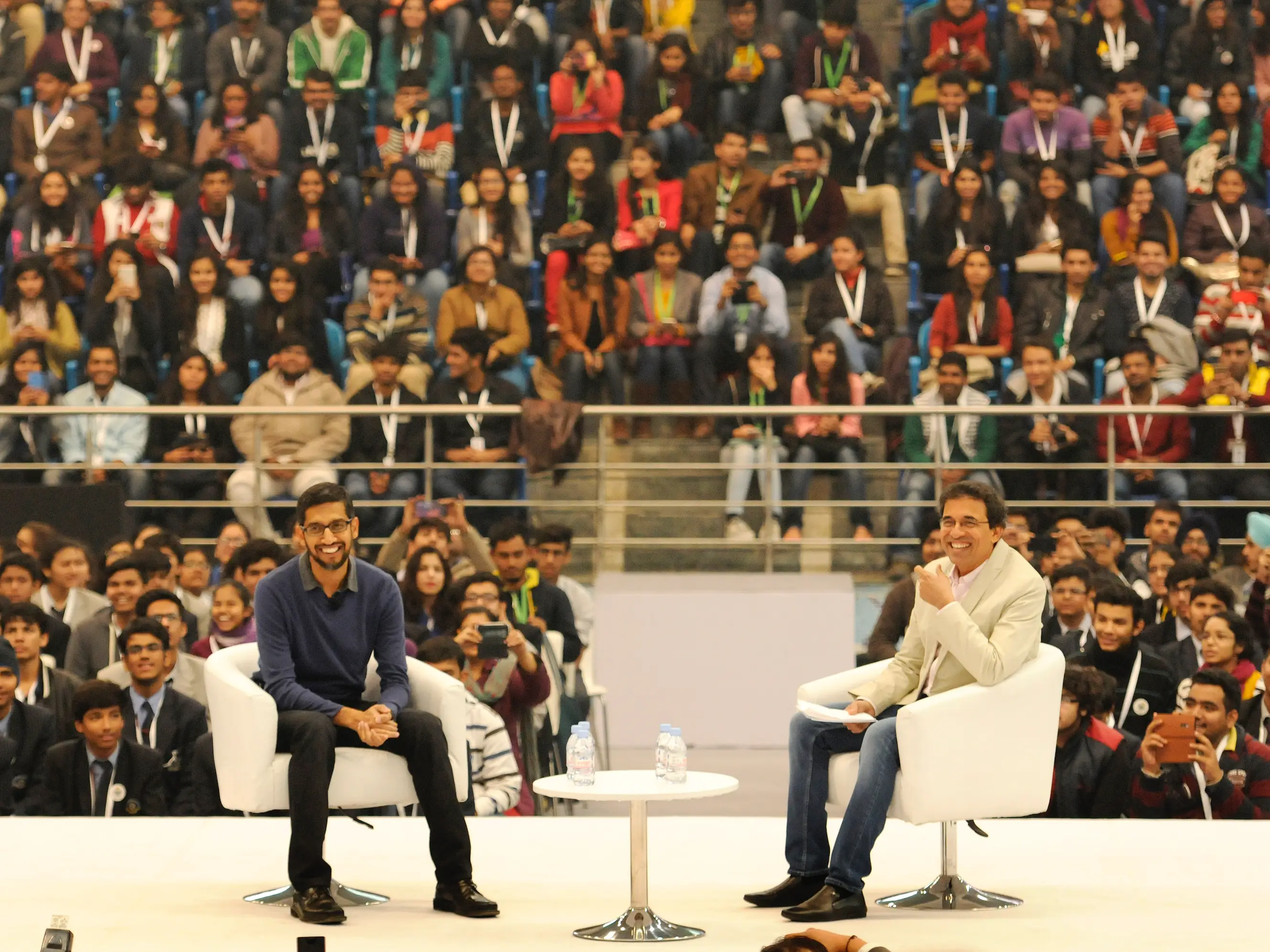 Google CEO Sundar Pichai smiles as he sits on a stage with interviewer Harsha Bhogle, in front of an audience in India.