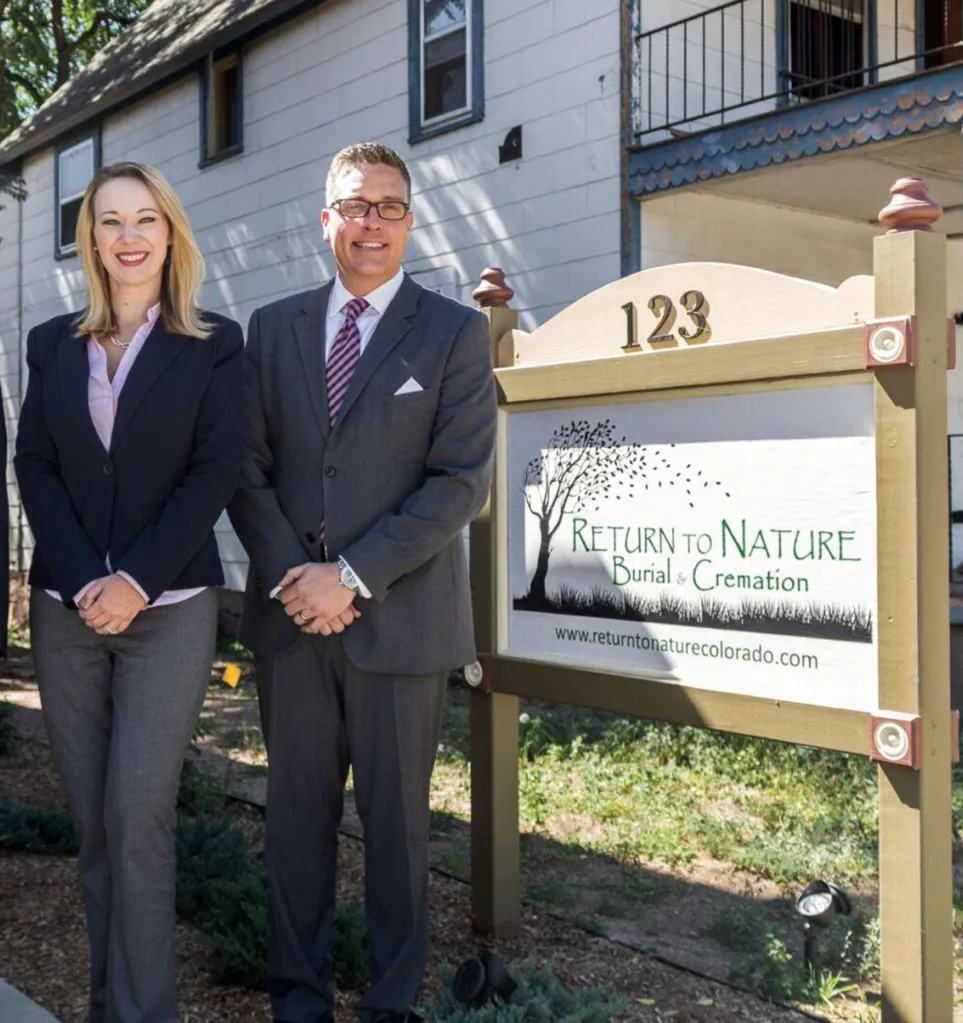 Two people smiling next to a sign for Return to Nature Burial & Cremation.