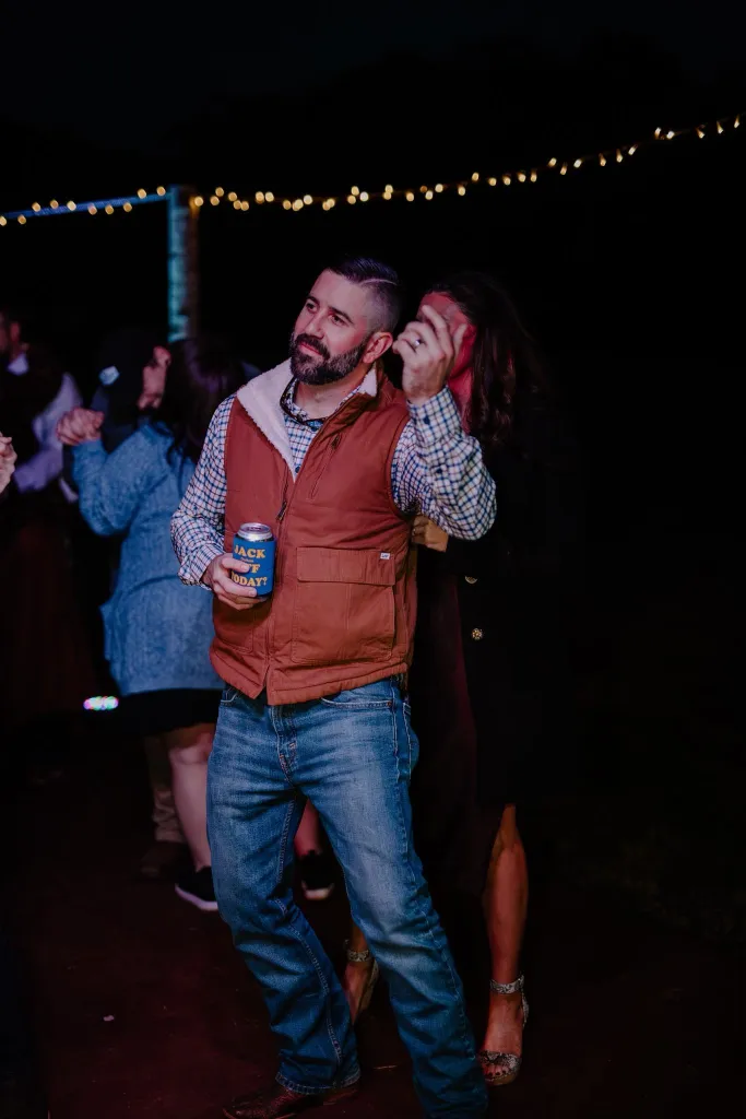 A man in a vest and plaid shirt holding a can of