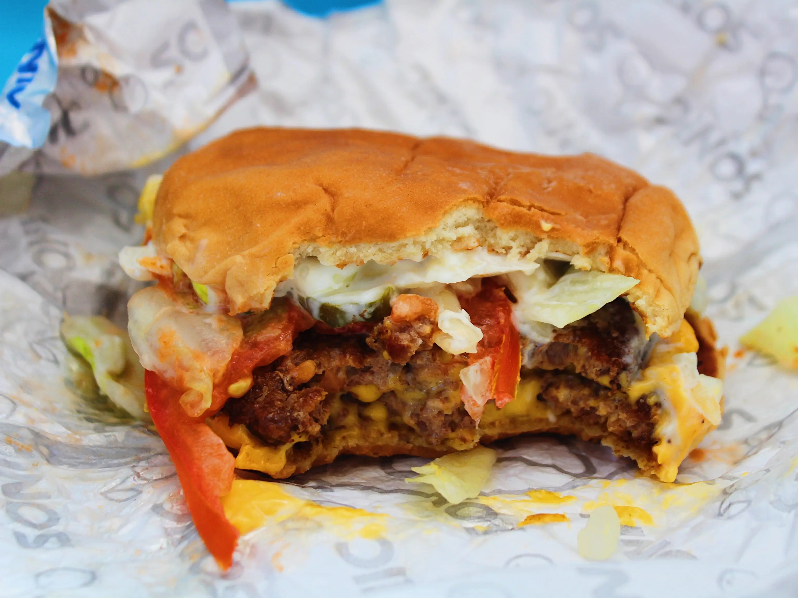 bitten into sonic double cheeseburger in tin foil wrapping on blue background