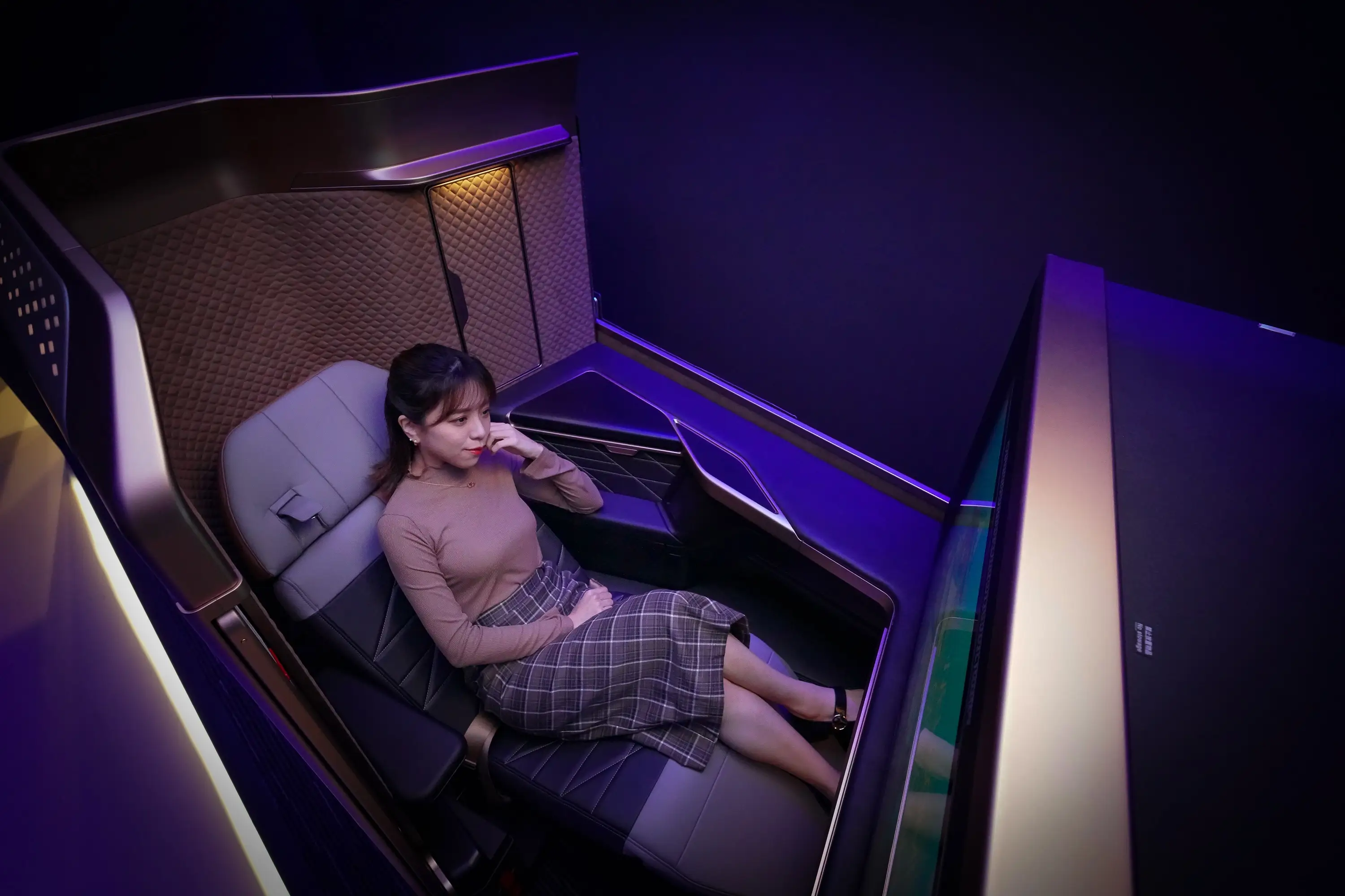 A person sitting in Starlux' first class partially reclined with blue ambiant lighting.