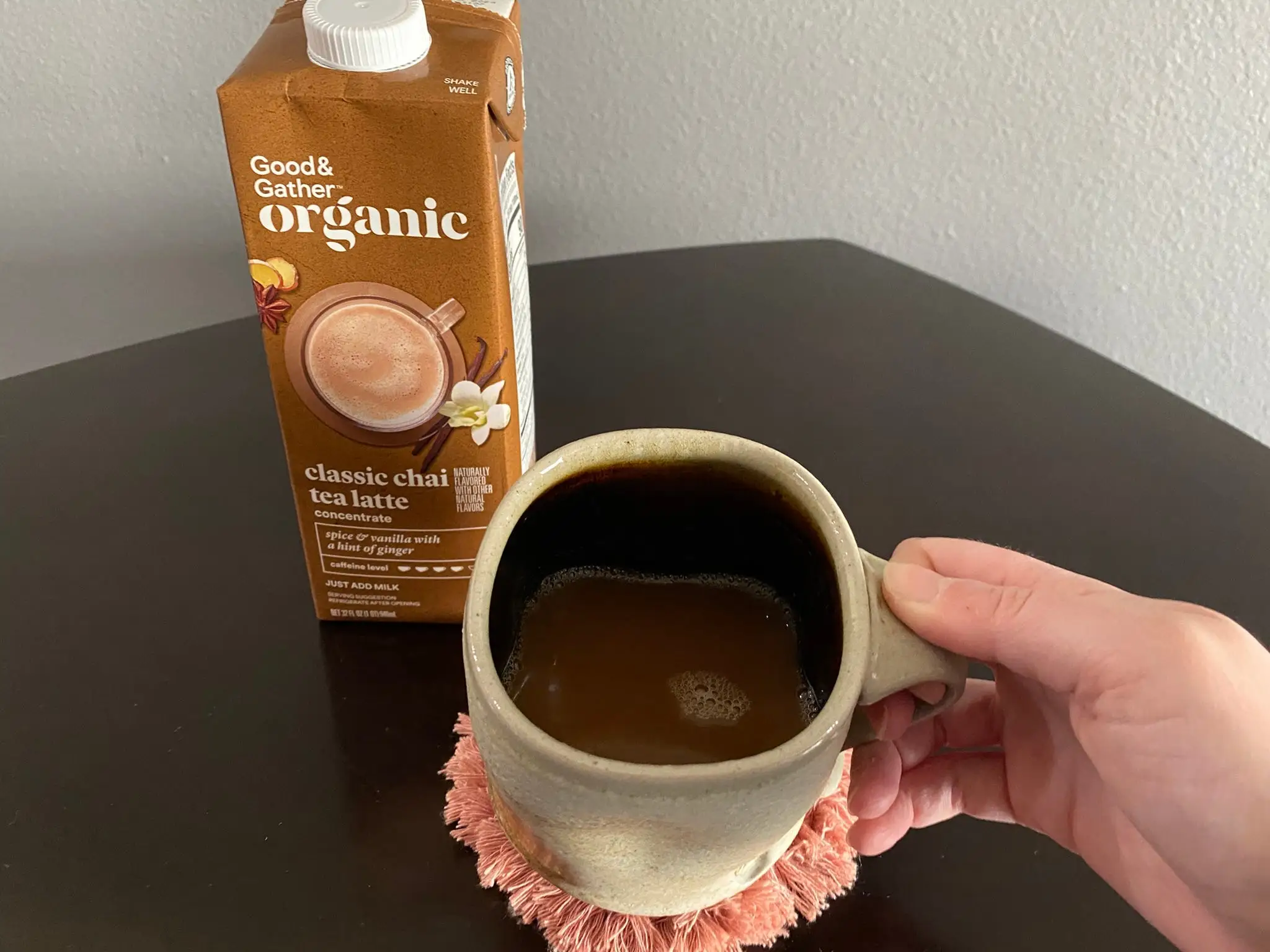 Brown carton of Good & Gather chai concentrate next to mug of hot chai latte held by author's hand.