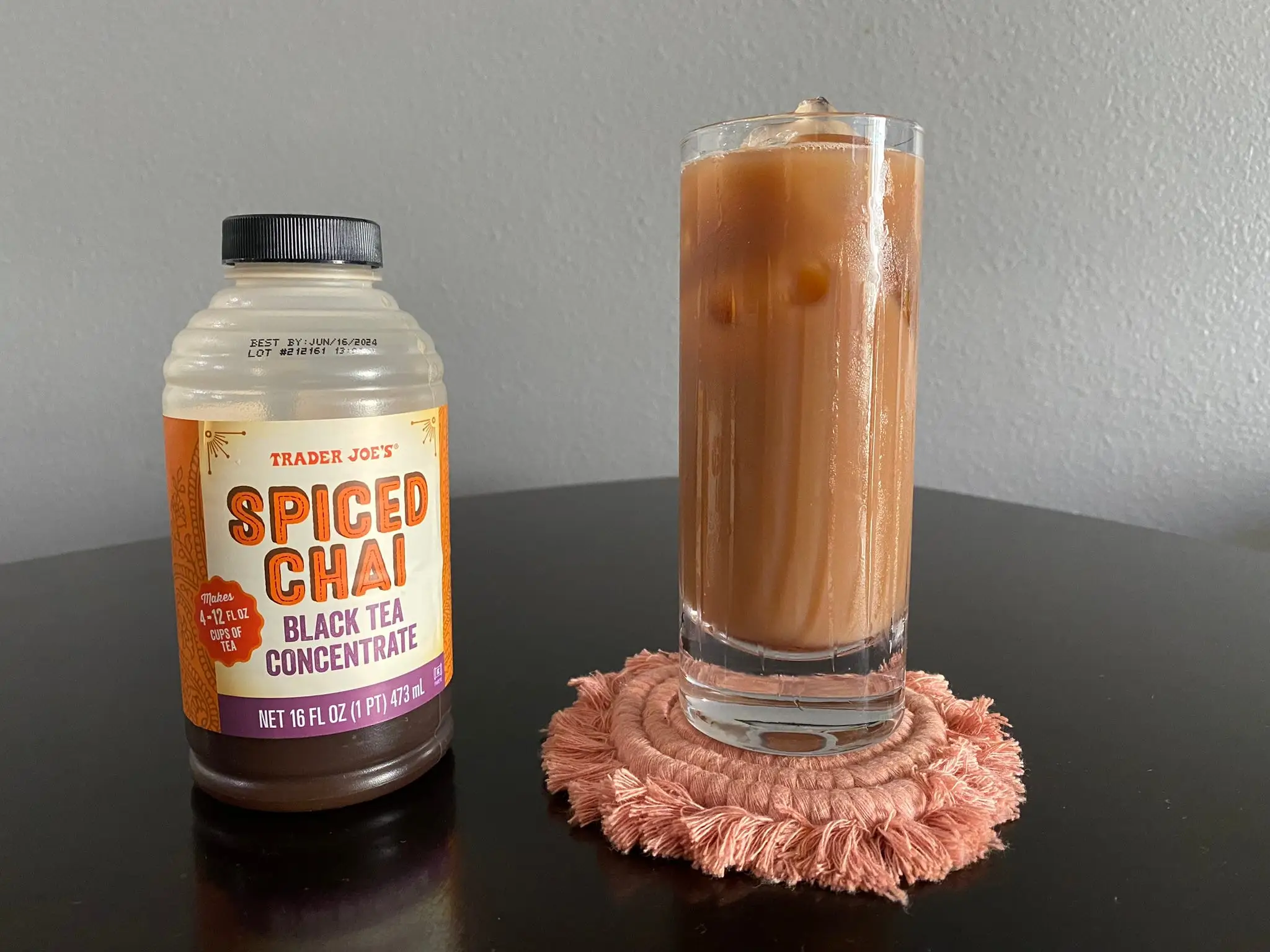 Trader Joe's container of chai concentrate next to tall glass of iced chai latte.