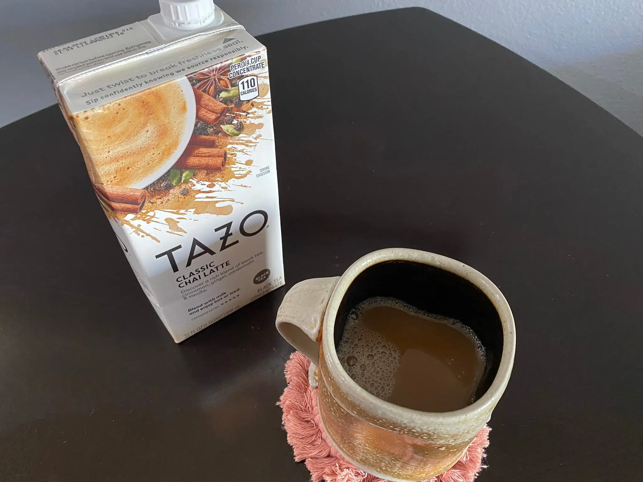 Tazo chai concentrate carton next to mug of hot chai latte.