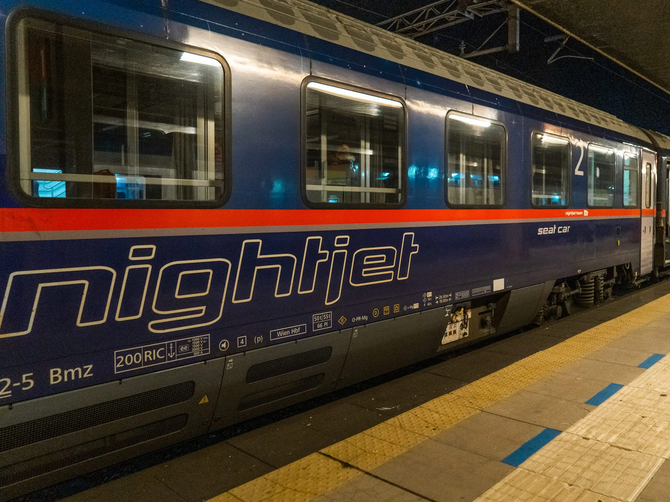 A blue train with a red stripe stopped at a platform at night