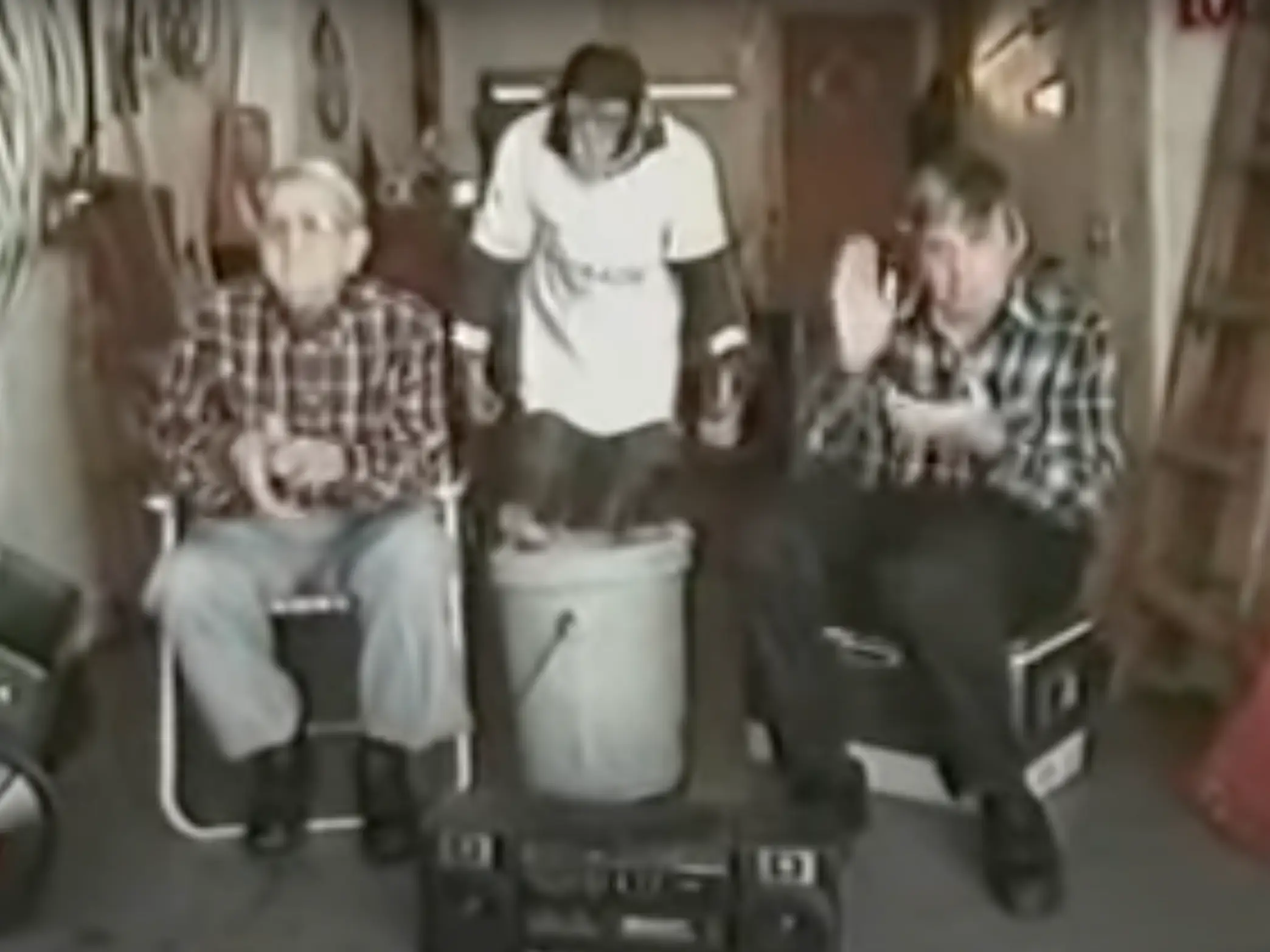 A monkey in a white shirt stands on a bucket between two men in lawn chairs.