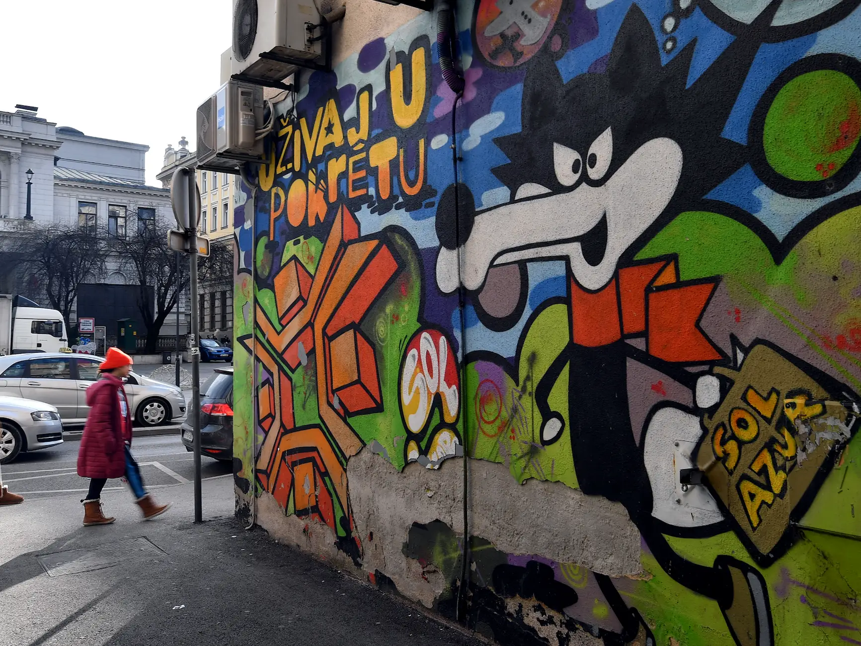 Pedestrians walk past graffiti depicting the official olympic mascot 