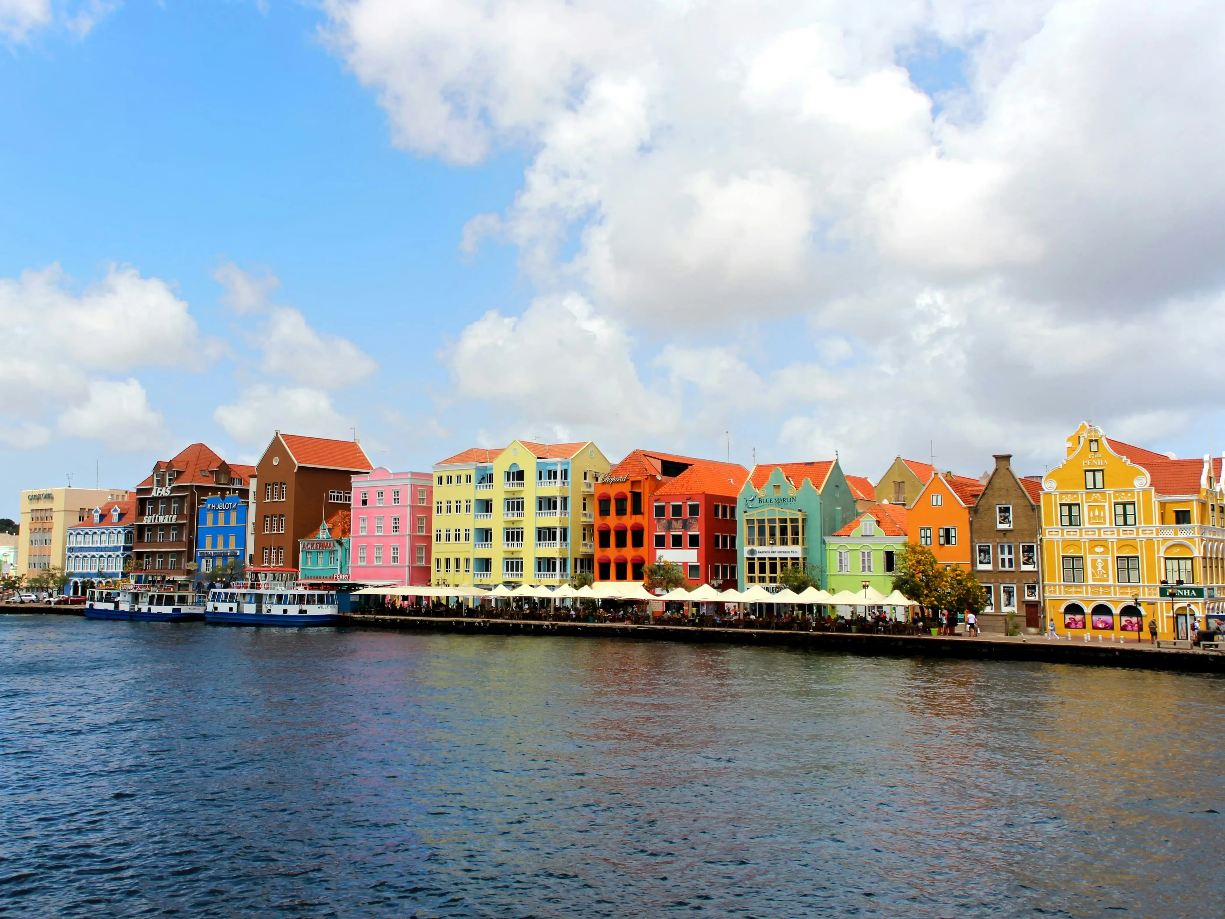 Several colorful houses, from blue to yellow to pink to green, lined along a waterfront.